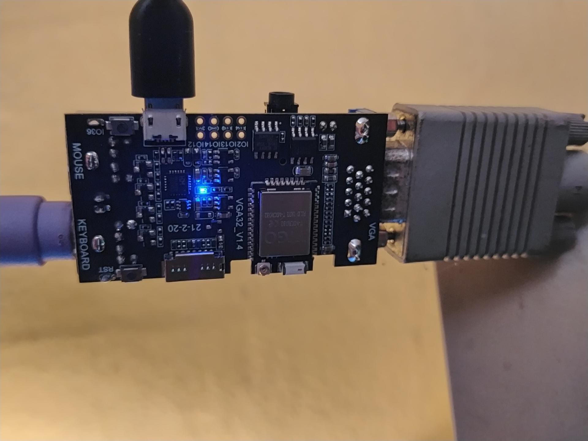 the LILYGO TTGO VGA32 board itself, with a blue LED, a VGA cable plugged in, and a USB to PS2 adaptor plugged in also.